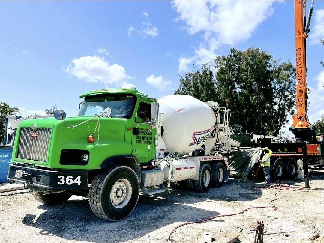 Caminhão betoneira verde 364 da Superior Mix ao lado de uma bomba lança laranja em uma obra no sul da Flórida, com um trabalhador de colete refletivo